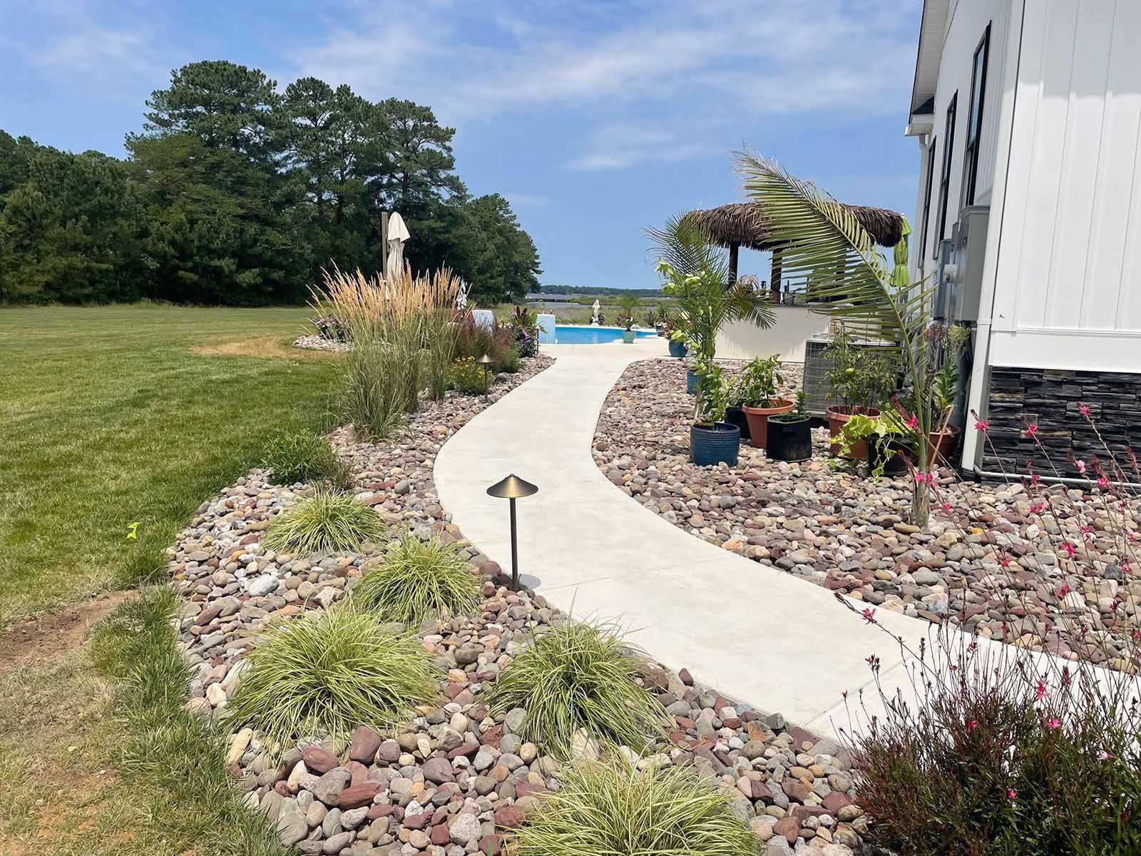 A concrete walkway leading to a house with a pool in the background