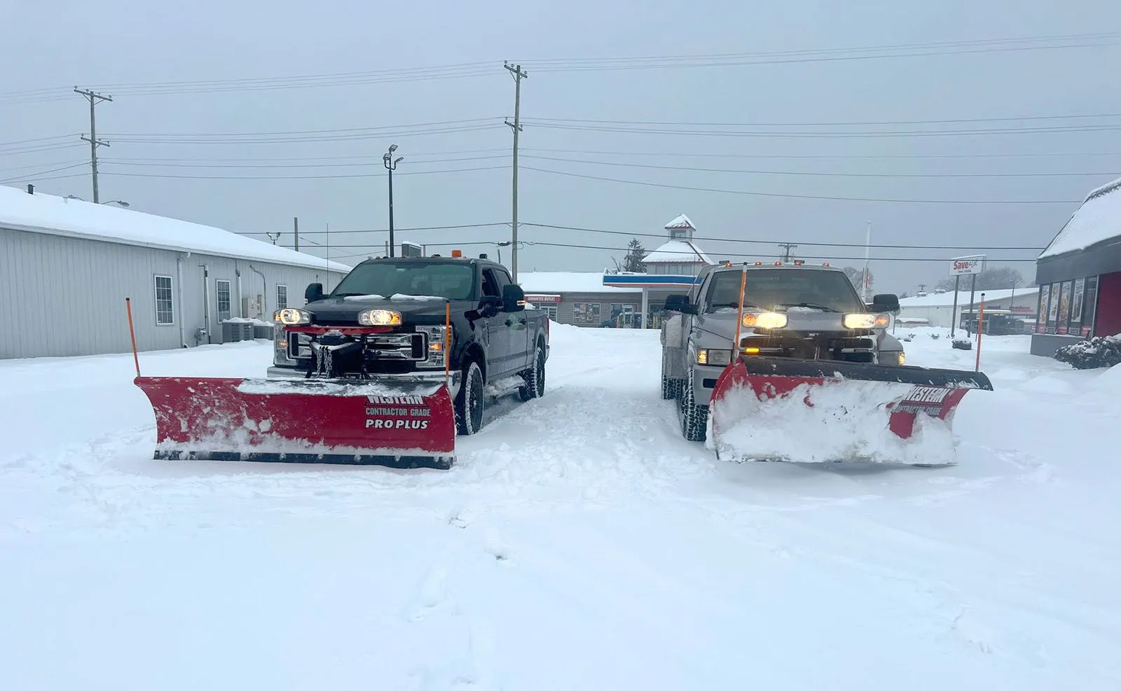 Two snow plowing trucks are parked next to each other in the snow