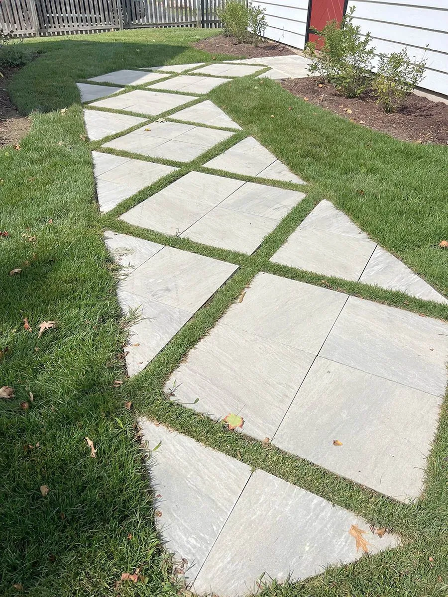 A concrete walkway surrounded by grass in front of a house